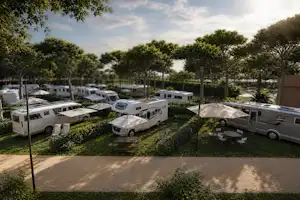 Wohnmobile auf einem Campingplatz-Stellplatz, gepflasterter Weg und Rasenflächen mit Bäumen im Hintergrund.