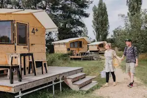 Wohnwagen mit Terrasse und Stufen auf einem Campingplatz, im Hintergrund weitere Unterkünfte und Bäume.