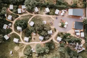 Luftaufnahme eines Campingplatzes mit vielen Stellplätzen, kleinen Wohnwagen und Zelten, Wegen und Bäumen im grünen Gelände.