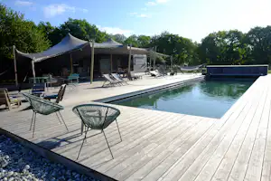 Holzterrasse mit Pool und Liegestühlen, im Hintergrund Zelte mit Sonnenschirmen und Sitzgelegenheiten am Campingplatz.