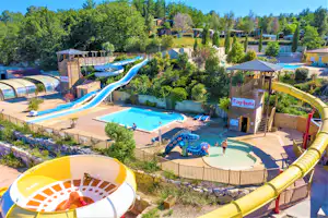Wasserrutsche und Poolbereich mit Liegen, Sonnenschirmen und Gartenwegen im Campingpark, umgeben von Bäumen und Zäunen.