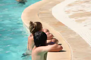 Familie am Poolrand: zwei Personen sitzen am Beckenrand, Wasser im Hintergrund.
