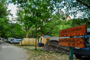 Schild „Allee du Verdon“ am Campingplatz, daneben Zelte und geparkte Autos im Grünen unter Bäumen.