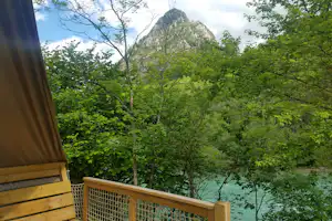 Blick vom Campingbalkon auf dichten Wald und einen Felsberg in der Ferne, umrahmt von grünen Bäumen.