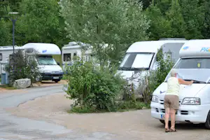 Wohnmobile auf dem Campingplatz, Hecken und lila Blumen am Weg, im Hintergrund Bäume und ein Mann am Fahrzeug.