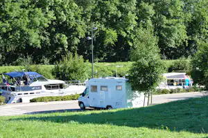 Wohnmobil und weitere Camper auf einem Campingplatz, umgeben von Bäumen und Hecken, mit Stellplatzstraße im Vordergrund.