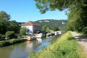 Blick auf den Fluss mit Booten und Stegen, daneben ein Campingplatz mit Gebäude und Bäumen im Grünen.