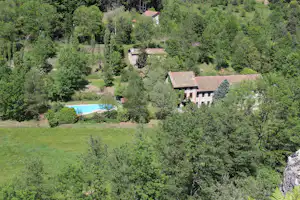Luftaufnahme eines Campingplatzes im grünen Tal mit Pool, mehreren Gebäuden und Wegen zwischen Bäumen und Wiesen.