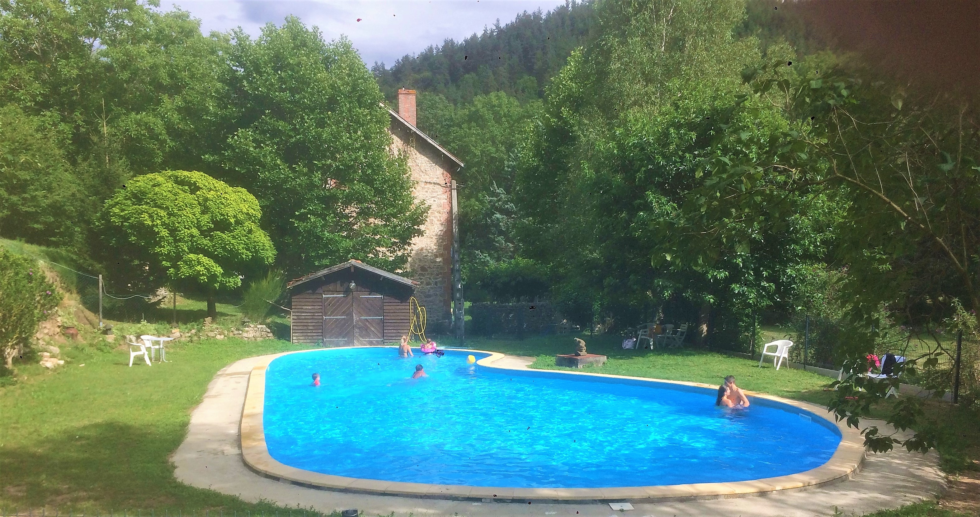 Blauer Camping-Pool im Garten mit Liegestühlen, Rasen und Bäumen; im Hintergrund ein Gebäude und ein kleiner Schuppen.