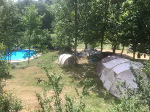 Zelte auf einem Campingplatz im Grünen, mit Bäumen, einem Weg und einem kleinen Pool im Hintergrund.
