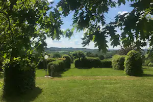 Grünes Camping-Panorama mit Wiese und Bäumen im Vordergrund, Blick auf Hügel und Felder in der Ferne.