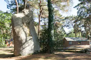 Großer Stein am Campingplatz vor einem Wohnwagen und Bäumen, mit Kiesweg und Rasenfläche im Hintergrund.