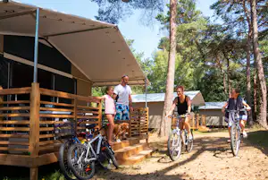 Holzterrasse am Campingplatz mit Zeltvorzelt, Fahrrädern und zwei Personen zwischen hohen Bäumen.