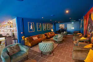 Blauer Innenraum mit Sitzgelegenheiten, Couchtisch und gepolsterten Sesseln, Wandbildern und beleuchteter Bar im Campinggebäude.