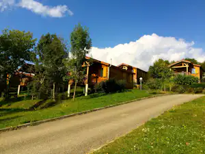 Reihen von Camping-Bungalows mit Holzveranda und Geländer, eingebettet in grünes Gelände neben einem breiten Weg.