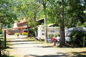 Wohnwagen und Wohnmobil stehen auf einem Campingplatz zwischen Bäumen, daneben ein Tisch mit Stühlen.
