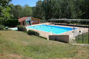 Beheizter Camping-Pool mit Umzäunung, Liegen und Sonnenschirmen, umgeben von Rasen und Bäumen.