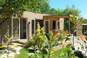 Modernes Holzhaus mit Terrasse, großen Fenstern und Liegestühlen im Garten mit Bäumen und Sträuchern.