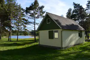 Ferienhaus mit Satteldach am Seeufer, umgeben von Bäumen und Rasenfläche auf dem Campingplatz.