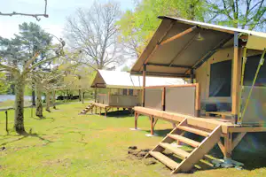 Mobilheim mit Veranda und Holztreppe auf einem Stellplatz, umgeben von Rasen und Bäumen im Campinggelände.