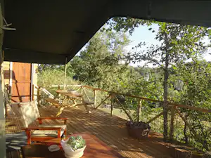Holzterrasse am Campingplatz mit Sitzbank, Tisch und Pflanzkübeln, Blick in den Garten mit Bäumen und Zaun.