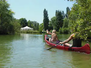Rotes Ruderboot auf dem See, im Hintergrund Zeltpavillon und Bäume am Ufer.