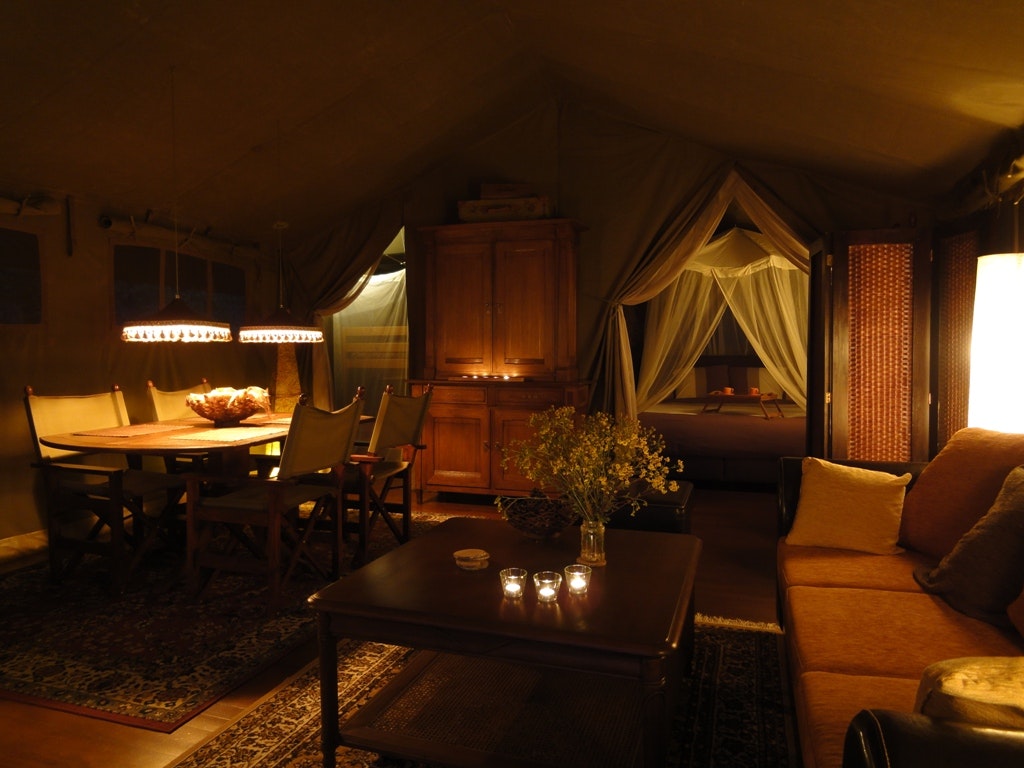 Wohnbereich im Campingzelt mit Sofa, Esstisch, Stühlen und Tischlampe, dekoriert mit Blumenstrauß und Lichterkette.