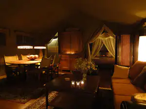 Wohnbereich im Campingzelt mit Sofa, Esstisch, Stühlen und Tischlampe, dekoriert mit Blumenstrauß und Lichterkette.