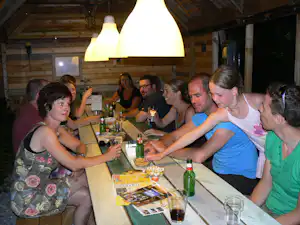 Gruppe beim gemeinsamen Abendessen am Holztisch in einer überdachten Campinghütte, mit Gläsern und Flaschen auf dem Tisch.
