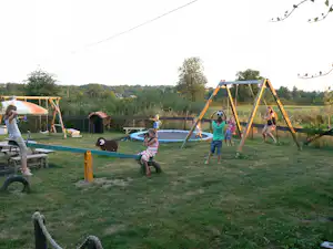 Spielplatz auf dem Campingplatz: Schaukelgerüst, Rasenfläche und Kinder beim Spielen, im Hintergrund ein Trampolin und ein Zelt.