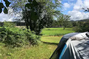 Campingzelt auf einer grünen Wiese im Campinggarten, umgeben von Bäumen und Sträuchern, mit Blick auf die Landschaft.
