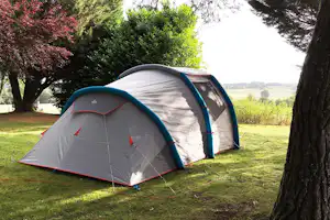 Zelt auf einem Campingplatz im Grünen, umgeben von Bäumen, mit Blick auf Wiesen und Felder in der Ferne.