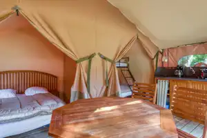 Glamping-Zelt mit Doppelbett, Holzbank und Küchenzeile im Innenbereich, Vorhänge und Holzwände sichtbar.