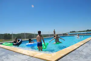 Camping-Pool mit mehreren Schwimmreifen, Personen im Wasser und am Beckenrand auf der Sonnenterrasse.