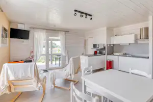 Heller Wohnbereich in einem Mobilheim mit Küchenzeile, Esstisch, weißen Stühlen und großen Fenstern zur Terrasse.