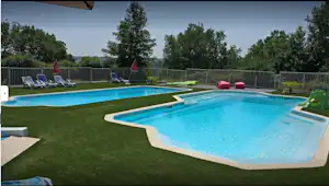 Zwei Camping-Schwimmbecken mit türkisfarbenem Wasser, Liegen am Rand und gepflegtem Rasen, umgeben von Zäunen und Bäumen.