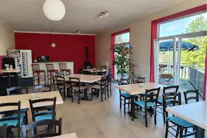 Innenraum eines Camping-Restaurants mit Tischen, Stühlen, Tresen und großen Fenstern zur Terrasse.