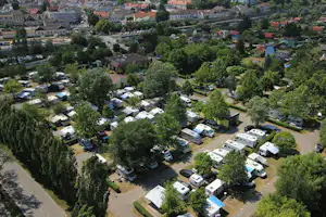 Luftaufnahme eines Campingplatzes mit Wohnmobilen und Wohnwagen auf Stellplätzen, umgeben von Bäumen und Straßen in der Nähe.