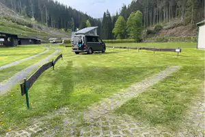 Wohnmobil auf einem Campingplatz-Stellplatz auf grüner Wiese, mit Rasengitter und niedrigen Holzpfosten, im Tal mit Bäumen.