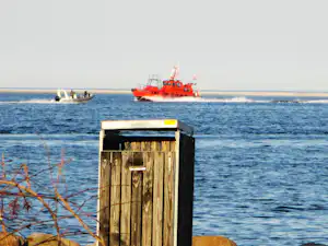 Rettungsboot und Beiboot auf dem Meer, im Vordergrund ein Holzschuppen am Strand.