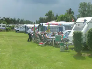 Campingplatz mit Wohnwagen und Zelten, davor ein Tisch mit Stühlen und Grill auf der Wiese.