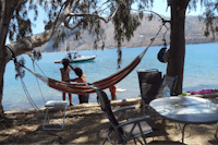 Elena's Beach Camping - Blick auf die ionische See vom Campingplatz, mit Sitzgelegenheiten im Vordergrund, einer Hängematte zwischen Bäumen und Anglern