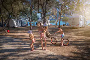 Elena's Beach Camping - Wohnwagen- und Zeltstellplatz mit Wohnmobilen zwischen Bäumen, Familie im Vordergrund