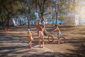 Elena's Beach Camping - Wohnwagen- und Zeltstellplatz mit Wohnmobilen zwischen Bäumen, Familie im Vordergrund