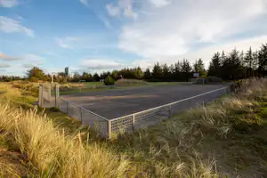 Tennisplatz auf dem Campingplatz mit Umzäunung, Grasflächen im Vordergrund und Bäumen am Rand.