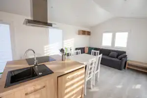 Moderne Wohnküche in einem Campinghaus mit Spüle, Herd, Esstisch und Sofa im hellen Raum.