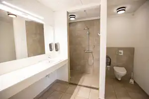Modernes Badezimmer mit Dusche, WC und Waschbecken im Campinghaus, hell gefliest und mit Spiegeln an der Wand.