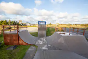 Wohnmobil-Stellplatz mit Betonfläche, Holzgeländern und einem großen Metallrohr im Vordergrund, im Hintergrund Schilder und Wege.