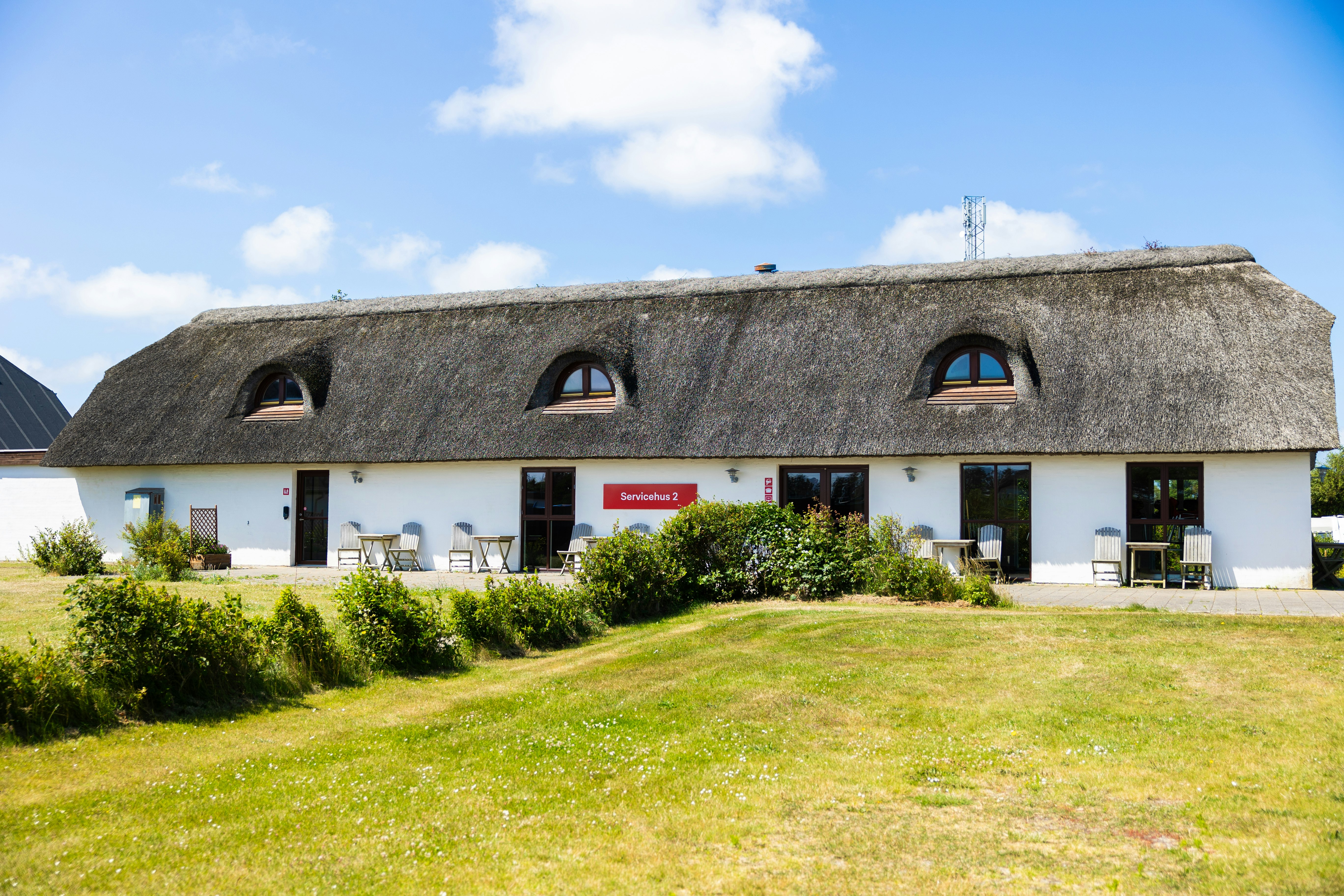 Reetgedecktes Ferienhaus mit drei Dachgauben, weißen Türen und Fenstern, davor Rasen und Hecken am Campingplatz.