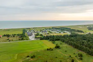 Luftaufnahme einer grünen Landschaft mit Campingplatz, Wegen und Häusern am Hang, Blick über Felder bis zum Meer.